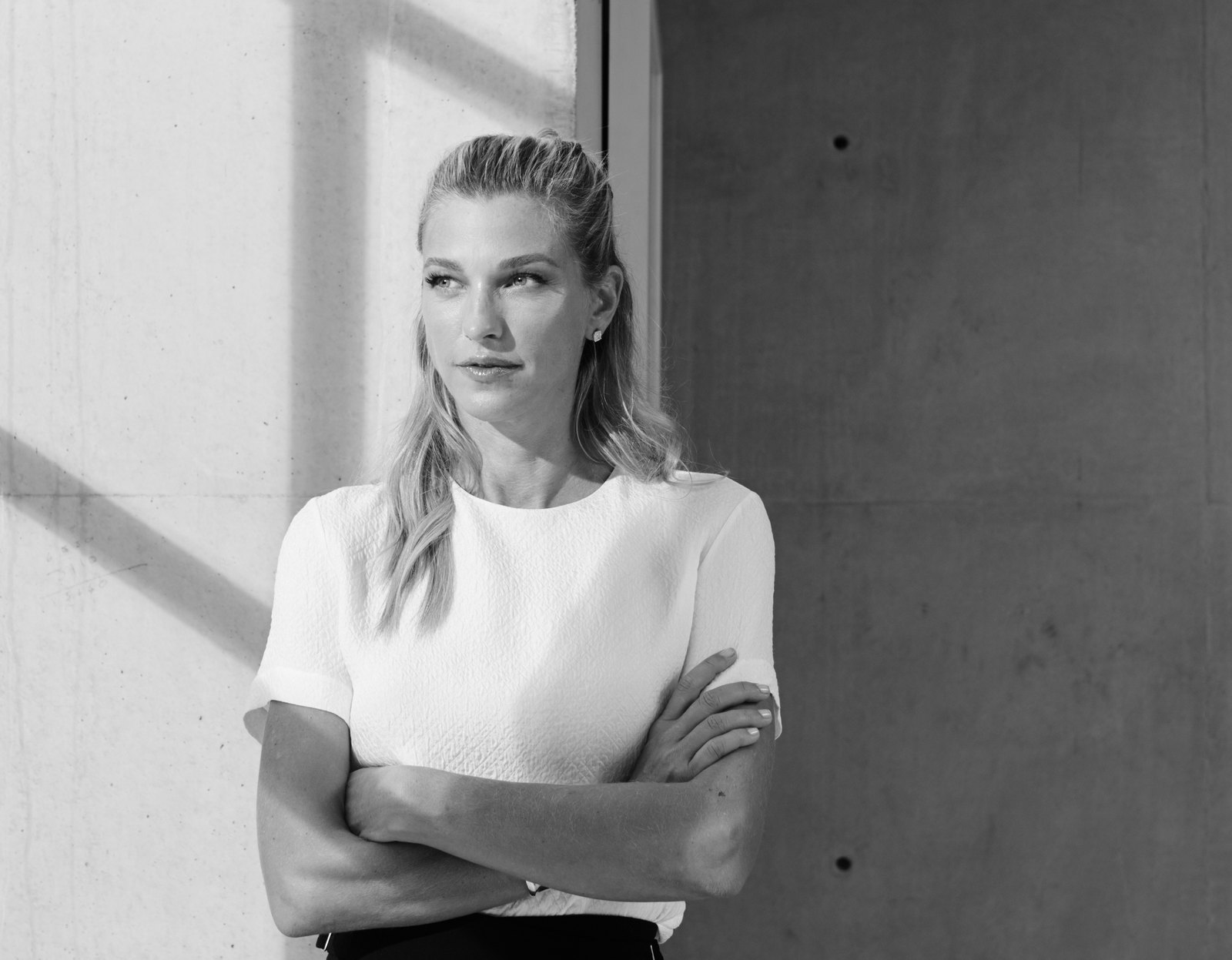 Nicole Junkermann in a white top, arms folded, standing in daylight beside a concrete wall